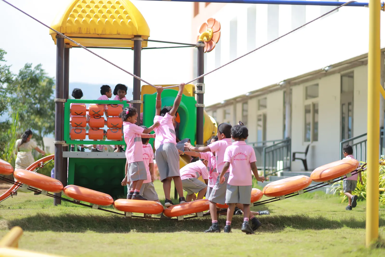 Young children play on the early-years garden climbing frame beside the school building