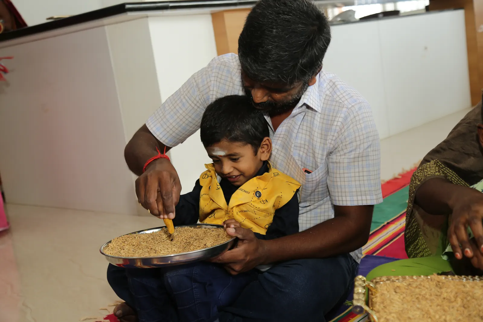 A father guides his son’s hand as he writes his first letter in rice