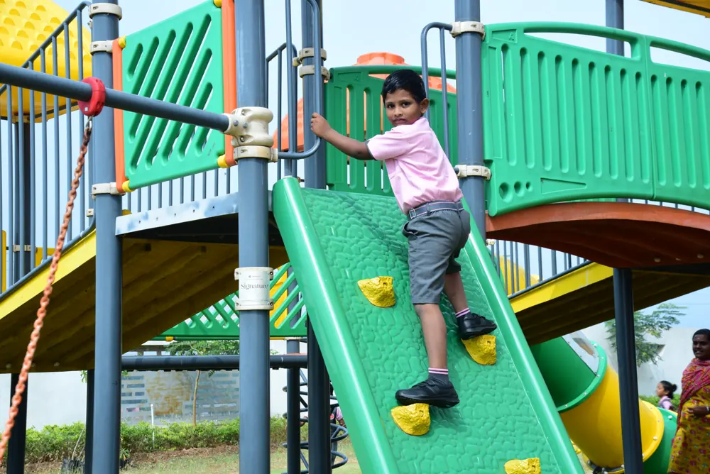 A young boy climbs a green rock wall on the playground