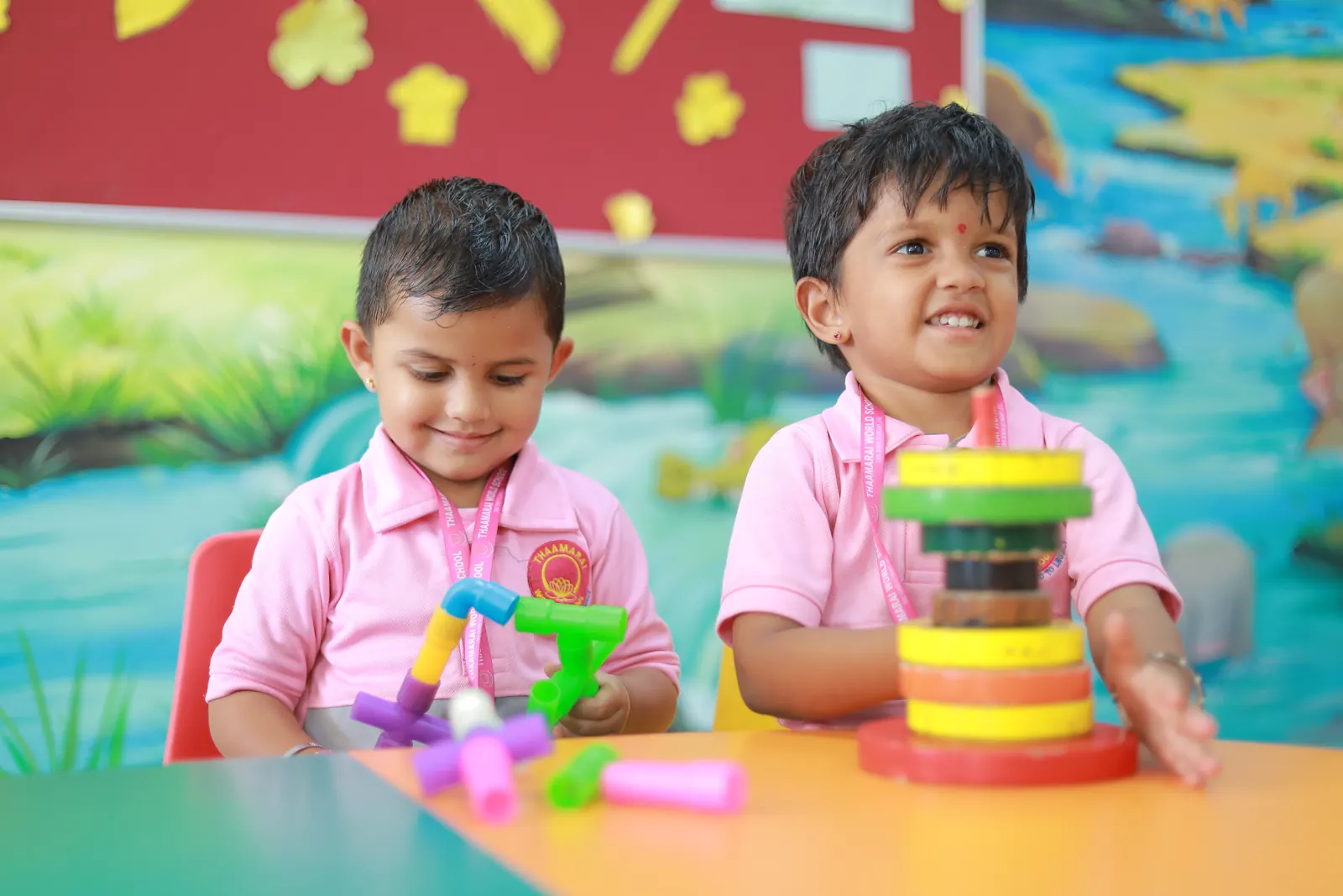 Two small boys in pink uniforms smile as they play with colourful stacking and building toys