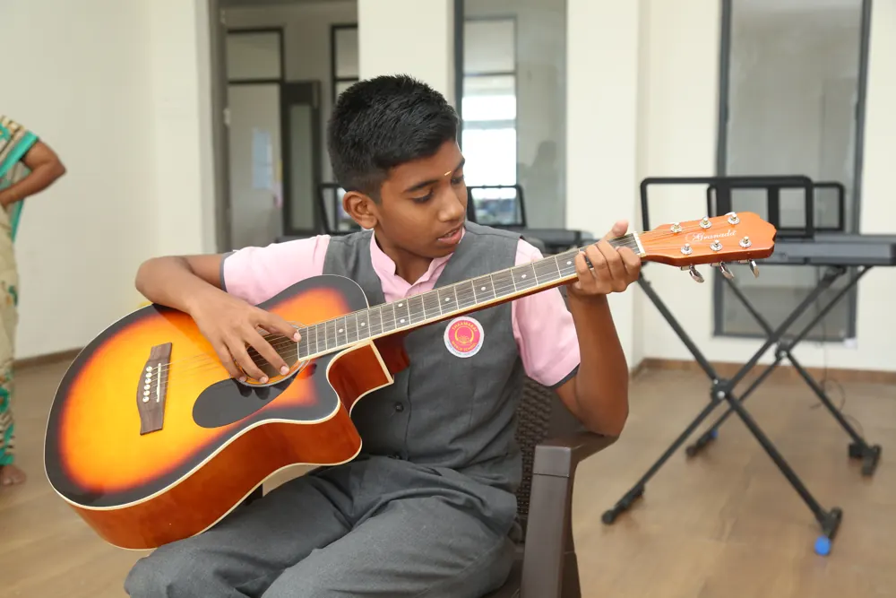 A boy plays an acoustic guitar in the music room