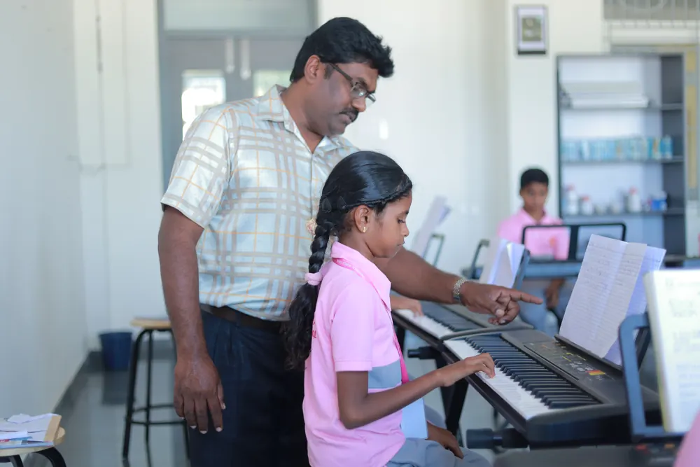A music teacher guides a girl at the keyboard