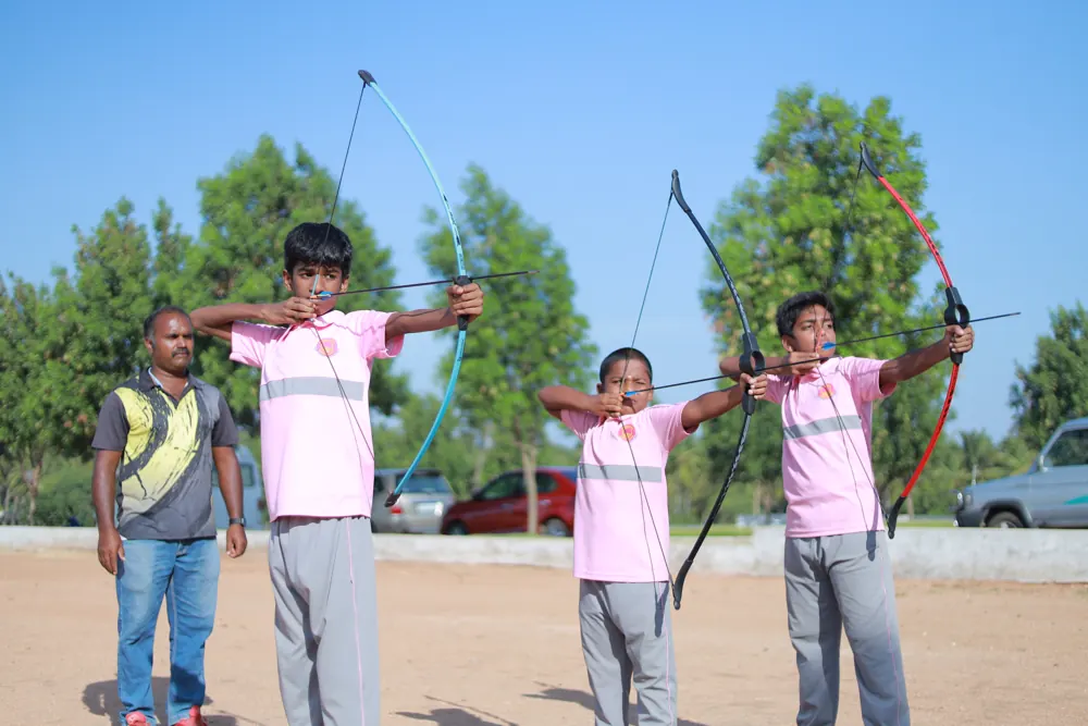 Three students draw their bows at archery practice