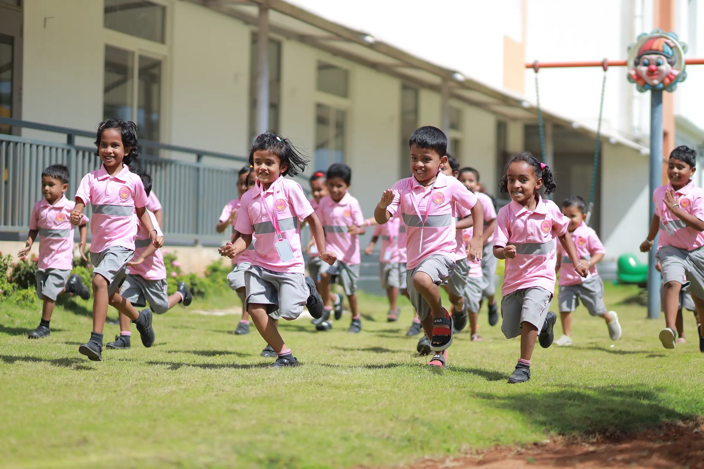 Kindergarten children in pink uniforms run joyfully across the green lawn towards the camera
