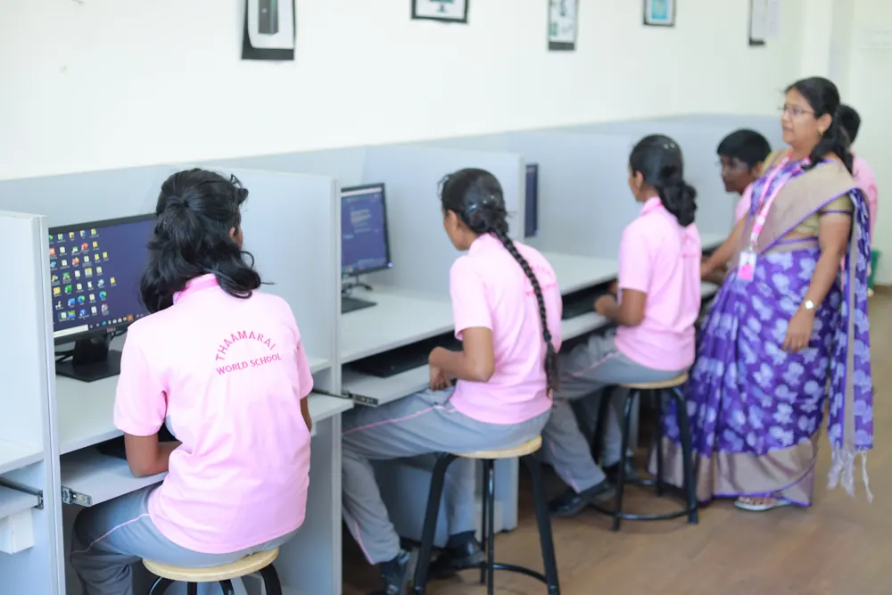 Students work at computers while their teacher helps