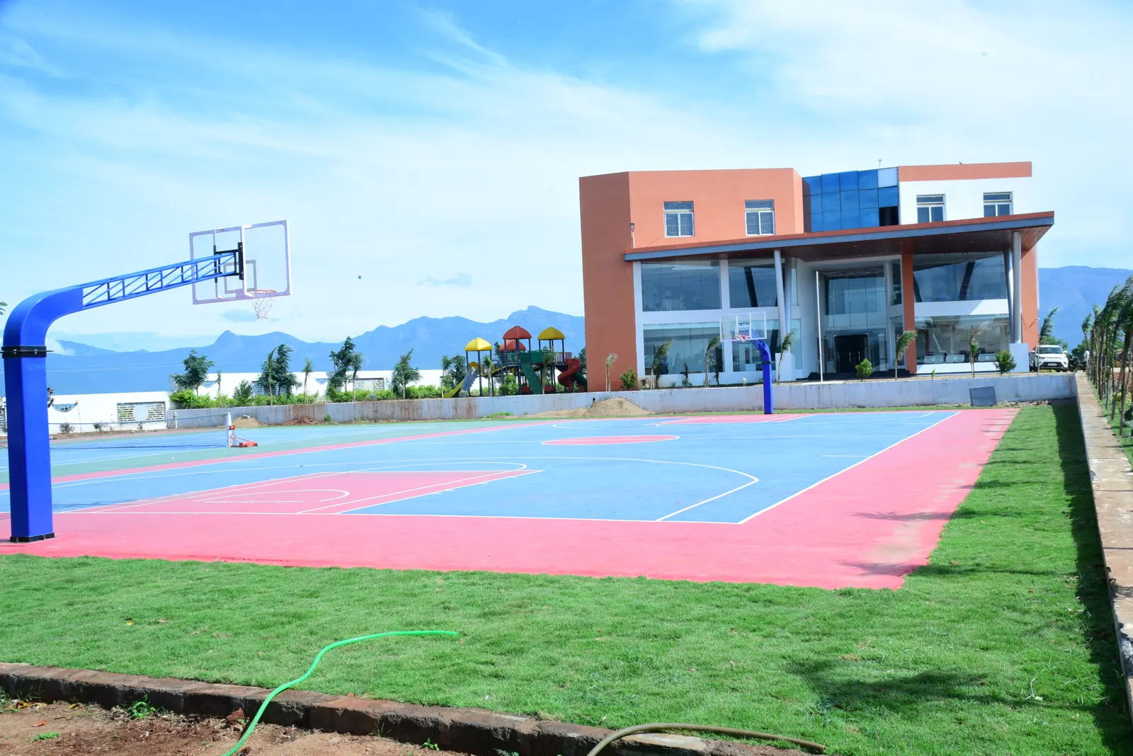 The basketball court and a school building on green lawn, with a range of hills on the horizon